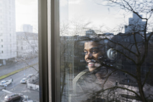 Man at window looking outside listening to music with headphones - SBOF00391