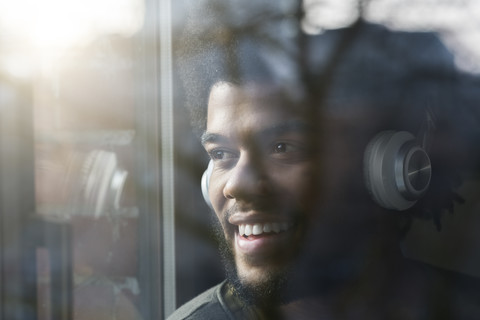 Mann am Fenster, der nach draußen schaut und mit Kopfhörern Musik hört, lizenzfreies Stockfoto