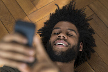 Lächelnder Mann auf dem Boden liegend mit Smartphone - SBOF00398