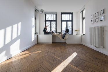 Smiling couple sitting in minimalist empty room talking - SBOF00431