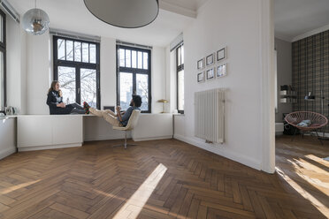 Smiling couple sitting in minimalist empty room talking - SBOF00432