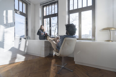 Smiling couple sitting in minimalist empty room talking - SBOF00433