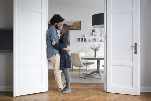 Küssendes Paar zu Hause im Türrahmen im Wohnzimmer stehend - SBOF00441