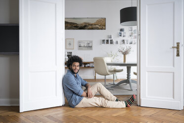 Man at home sitting on floor leaning on door frame in living room - SBOF00443