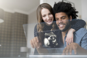 Smiling couple looking at ultra sound picture of baby on futuristic screen - SBOF00451