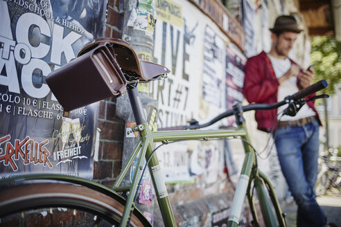 Germany, Hamburg, St. Pauli, Man using smartphone with bicycle in foreground - RORF00818