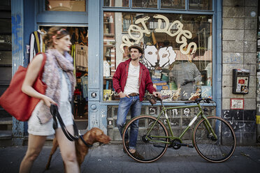Germany, Hamburg, St. Pauli, Man with bicycle waiting in front of vintage shop, woman with dog coming out - RORF00823