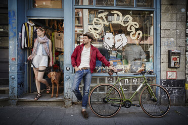 Germany, Hamburg, St. Pauli, Man with bicycle waiting in front of vintage shop, woman with dog coming out - RORF00825