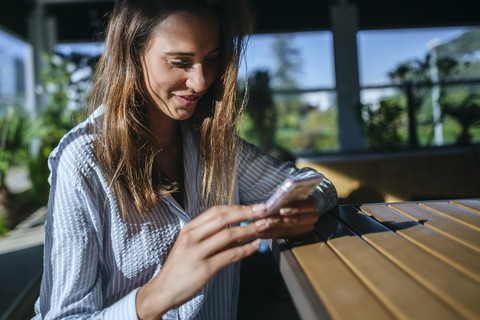 Lächelnde Frau auf Terrasse schaut auf Handy, lizenzfreies Stockfoto