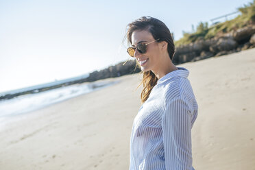 Lächelnde junge Frau mit Sonnenbrille am Strand - KIJF01454