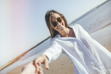 Porträt einer lächelnden jungen Frau mit Sonnenbrille, die ihre Hand am Strand hält - KIJF01455