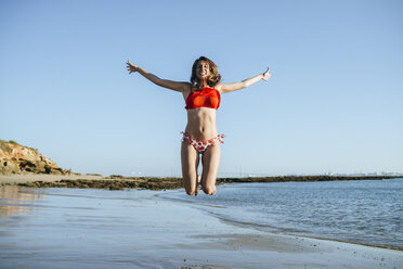 Lächelnde junge Frau, die am Strand in die Luft springt - KIJF01460