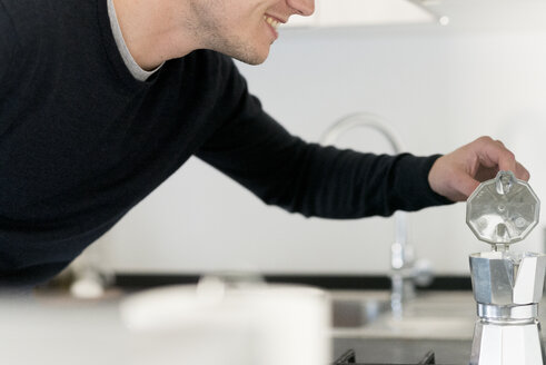 Lächelnder Mann bei der Zubereitung von Espresso in der Küche, Teilansicht - FMOF00251