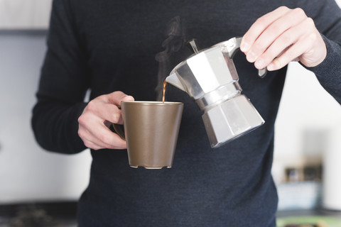 Man pouring hot espresso in a mug, partial view stock photo