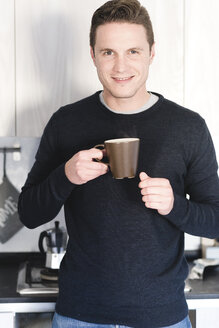 Porträt eines lächelnden Mannes mit einer Tasse Kaffee in der Küche - FMOF00254