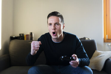 Portrait of screaming man sitting on the couch with games console - FMOF00263