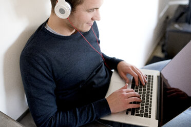 Mann benutzt Laptop und Kopfhörer zu Hause - FMOF00268