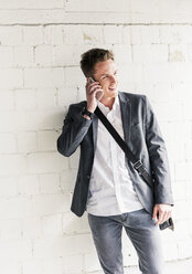 Young businessman using smartphone, standing in front of wall - UUF10590