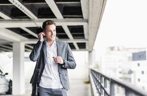 Young businessman using smartphone, walking on parking level - UUF10592