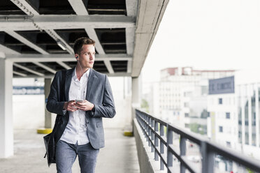 Junger Geschäftsmann, der ein Smartphone benutzt und auf einem Parkdeck spazieren geht - UUF10594