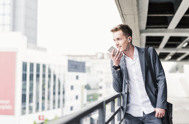 Young businessman using smartphone, standing on parking level - UUF10595