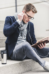Junger Geschäftsmann sitzt auf einer Treppe und benutzt ein digitales Tablet - UUF10601