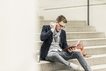 Young businessman sitting on stairs, using digital tablet - UUF10602