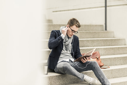 Junger Geschäftsmann sitzt auf einer Treppe und benutzt ein digitales Tablet - UUF10602