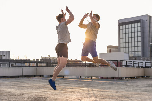 Freunde spielen Basketball bei Sonnenuntergang auf einer Dachterrasse - UUF10631