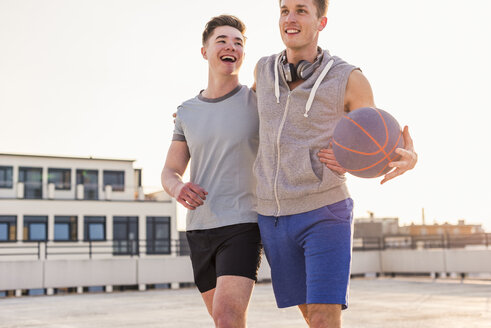 Freunde spielen Basketball bei Sonnenuntergang auf einer Dachterrasse - UUF10633