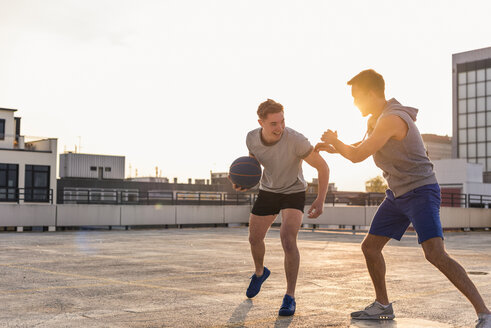 Freunde spielen Basketball bei Sonnenuntergang auf einer Dachterrasse - UUF10635