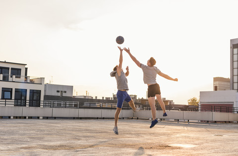 Freunde spielen Basketball bei Sonnenuntergang auf einer Dachterrasse, lizenzfreies Stockfoto