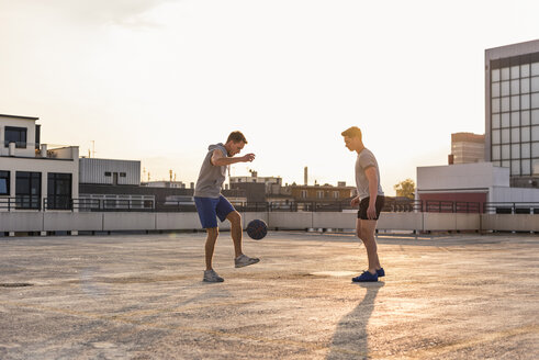 Freunde spielen Basketball bei Sonnenuntergang auf einer Dachterrasse - UUF10637