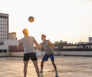 Freunde spielen Basketball bei Sonnenuntergang auf einer Dachterrasse - UUF10638