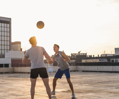 Freunde spielen Basketball bei Sonnenuntergang auf einer Dachterrasse - UUF10638