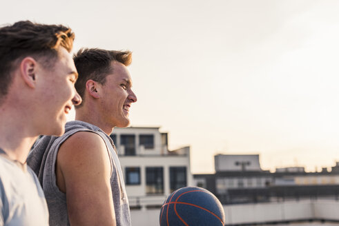 Freunde spielen Basketball bei Sonnenuntergang auf einer Dachterrasse - UUF10640