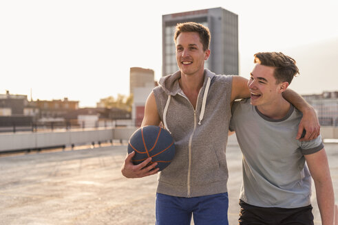 Freunde spielen Basketball bei Sonnenuntergang auf einer Dachterrasse - UUF10641