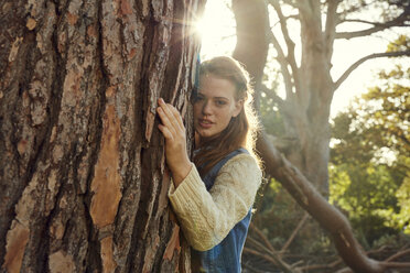 Portrait of young woman hugging tree at backlight - SRYF00431