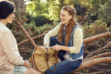 Zwei junge Frauen sitzen und sprechen auf einem Baumstamm - SRYF00436