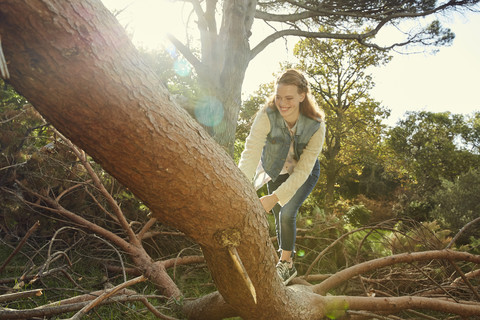 Lächelnde junge Frau, die auf einen Baumstamm klettert, lizenzfreies Stockfoto