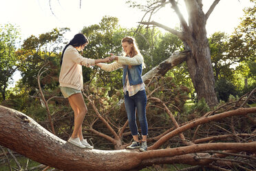 Two young woman balancing on tree trunk - SRYF00440