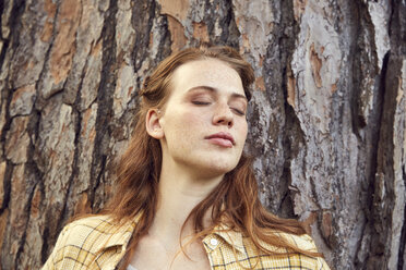 Portrait of redheaded young woman leaning against tree trunk with eyes closed - SRYF00452