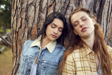 Porträt von zwei jungen Frauen, die sich mit geschlossenen Augen an einen Baumstamm lehnen - SRYF00453