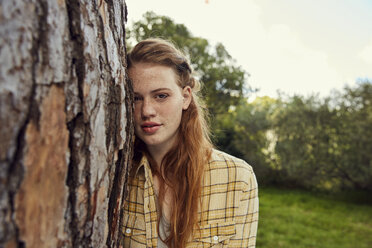Porträt einer jungen Frau, die sich an einen Baumstamm lehnt - SRYF00456