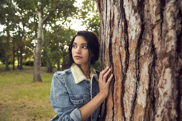 Porträt einer jungen Frau, die sich an einen Baumstamm lehnt - SRYF00459
