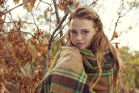 Porträt einer rothaarigen jungen Frau, eingewickelt in eine Decke in herbstlicher Natur, lizenzfreies Stockfoto