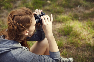 Young woman sitting on a meadow using binoculars - SRYF00490