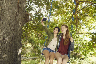 Zwei beste Freunde sitzen zusammen auf einer Schaukel und machen ein Selfie mit ihrem Smartphone - SRYF00496