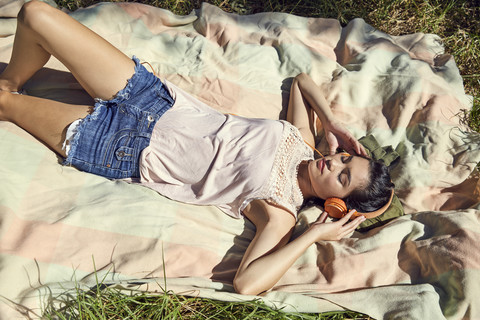 Junge Frau liegt auf einer Decke und hört Musik mit Kopfhörern, lizenzfreies Stockfoto