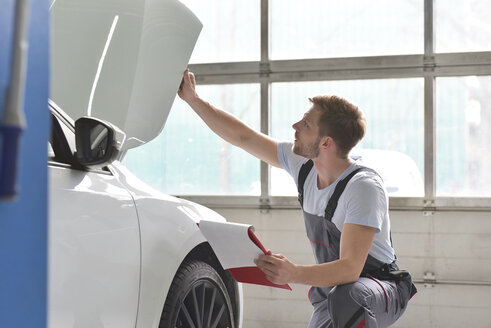 Automechaniker in einer Werkstatt, der ein Auto untersucht - LYF00686